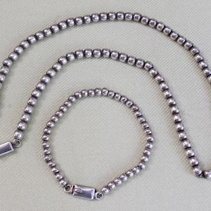 Peut inclure: Un ensemble de deux colliers de perles argentées, l'un plus long que l'autre. Les deux colliers ont un design simple et classique et sont faits de petites perles rondes.