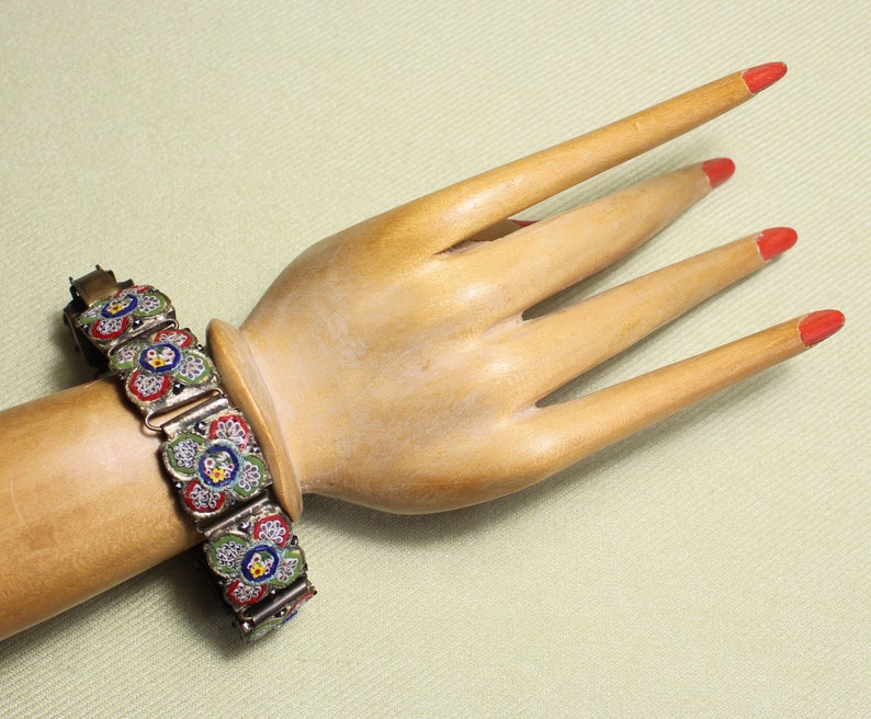 May include: A silver bracelet with a floral design made of colorful mosaic tiles. The bracelet is made up of several connected links, each featuring a different floral pattern.
