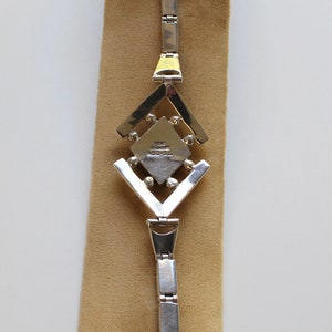 May include: A silver bracelet with a geometric design and a small square charm with the text "925 STERLING MEXICO" on it.