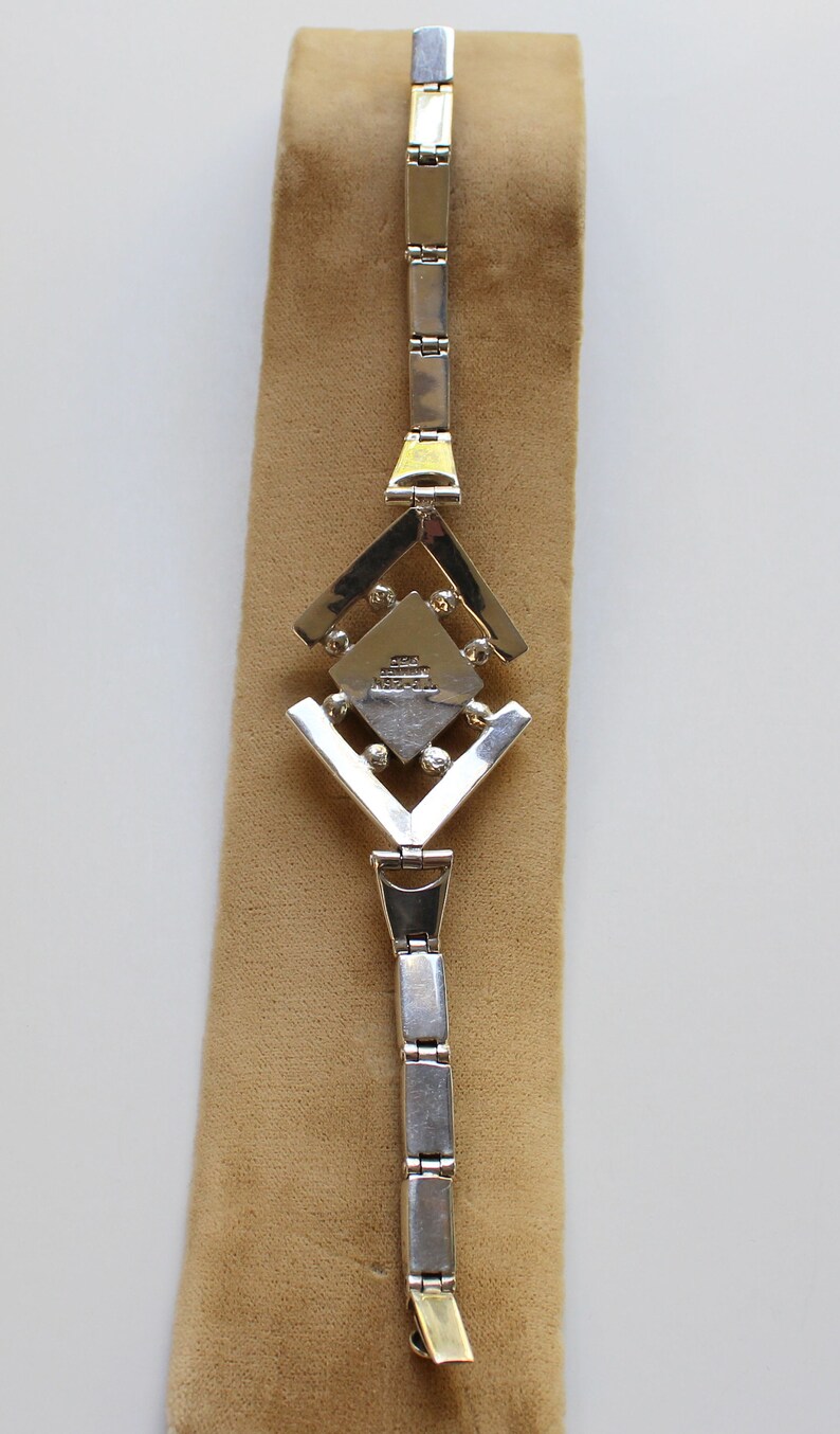 May include: A silver bracelet with a geometric design and a small square charm with the text "925 STERLING MEXICO" on it.