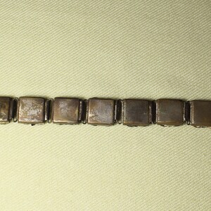 May include: A gold-toned bracelet with a chain link design. The bracelet is made up of square-shaped links with a smooth, slightly worn finish.