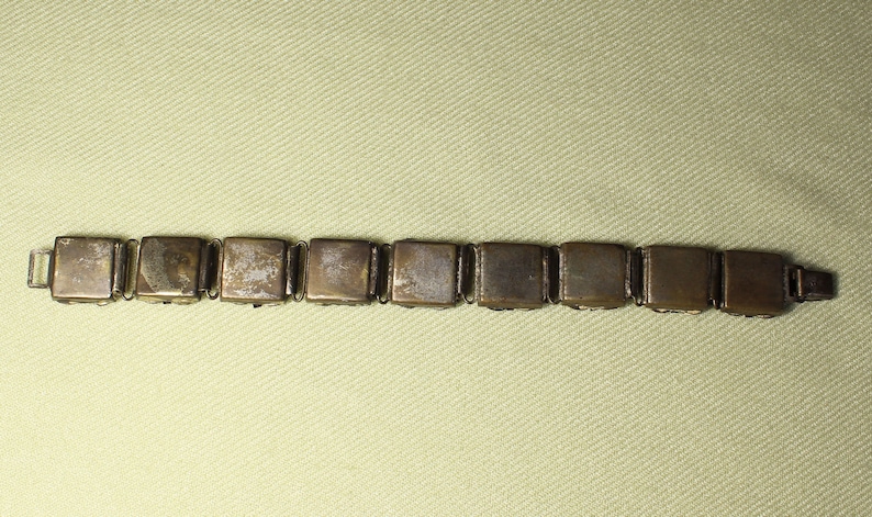 May include: A gold-toned bracelet with a chain link design. The bracelet is made up of square-shaped links with a smooth, slightly worn finish.