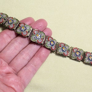 May include: A vintage bracelet with a floral design. The bracelet is made of metal and has a mosaic of small, colorful tiles. The tiles are arranged in a pattern of flowers. The bracelet is a beautiful example of vintage jewelry.