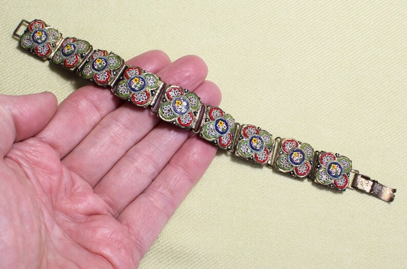 May include: A vintage bracelet with a floral design. The bracelet is made of metal and has a mosaic of small, colorful tiles. The tiles are arranged in a pattern of flowers. The bracelet is a beautiful example of vintage jewelry.