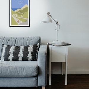 Room setting with a grey couch and side table with lamp. One the wall is a beautiful vintage style poster artwork of a cyclist on Sa Calobra, a famous cycling climb in Mallorca.