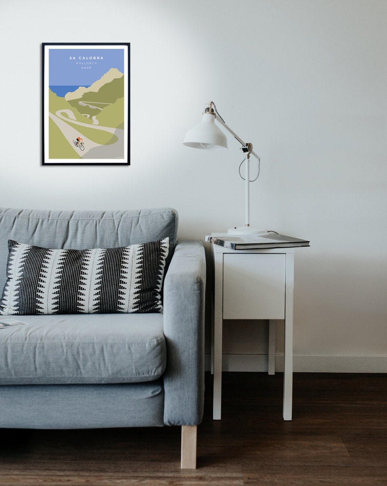 Room setting with a grey couch and side table with lamp. One the wall is a beautiful vintage style poster artwork of a cyclist on Sa Calobra, a famous cycling climb in Mallorca.