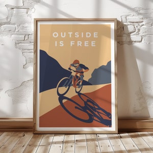 May include: A poster with a mountain biking scene and the text "OUTSIDE IS FREE". The poster has a brown background with a blue and orange mountain scene. The biker is wearing a helmet and riding a mountain bike.