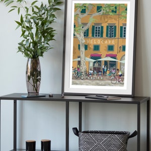 Velocafe cycling themed print showed framed and in a room environment on a black shelf with a vase and plant.