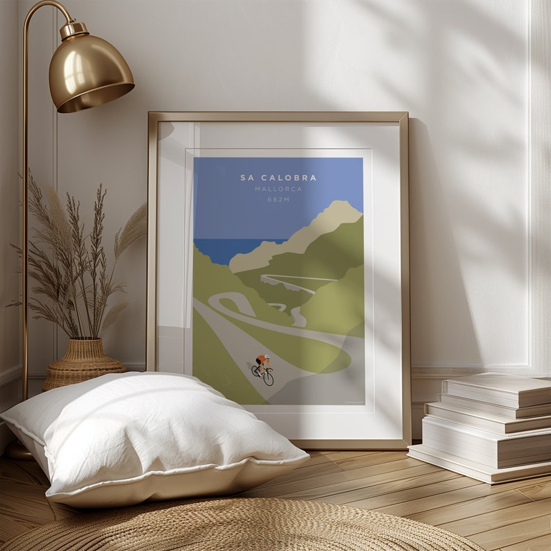 May include: A framed poster with a minimalist illustration of a cyclist riding up a winding road in the mountains. The poster is titled "Sa Calobra, Mallorca, 682m".