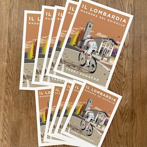 May include: A stack of eight cycling posters with a brown background and a cyclist riding a bicycle on a road with a church in the background. The text on the poster reads "IL LOMBARDIA MADONNA DEL GHISALLO TADEJ POGAČAR".