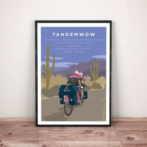 Framed art print leaning against a wall. TandemWoW Guinness World Record Holders Cycling Print showing the women tandem cyclists riding through a desert with cacti and mountains on their world record breaking challenge.