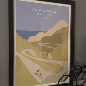 Sa Calobra Mallorca cycling art print shown framed in room setting with a cyclist ornament in the foreground on the shelf.