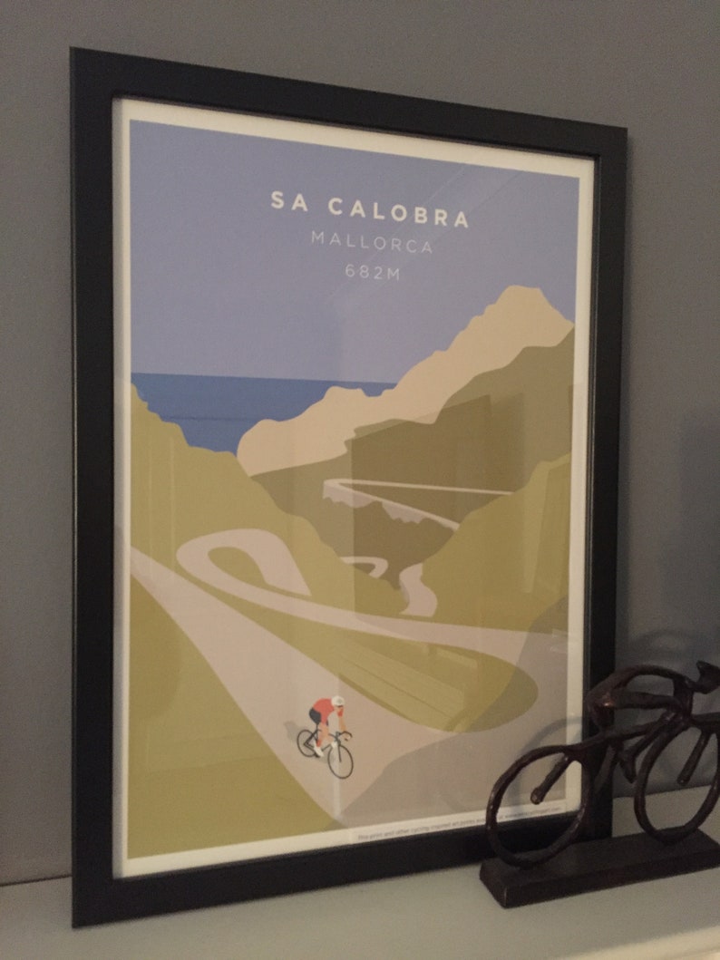 Sa Calobra Mallorca cycling art print shown framed in room setting with a cyclist ornament in the foreground on the shelf.