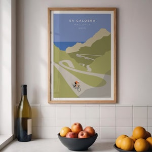 May include: A framed poster with a minimalist illustration of a cyclist riding up a winding road in the mountains. The poster is titled "Sa Calobra, Mallorca, 682m".