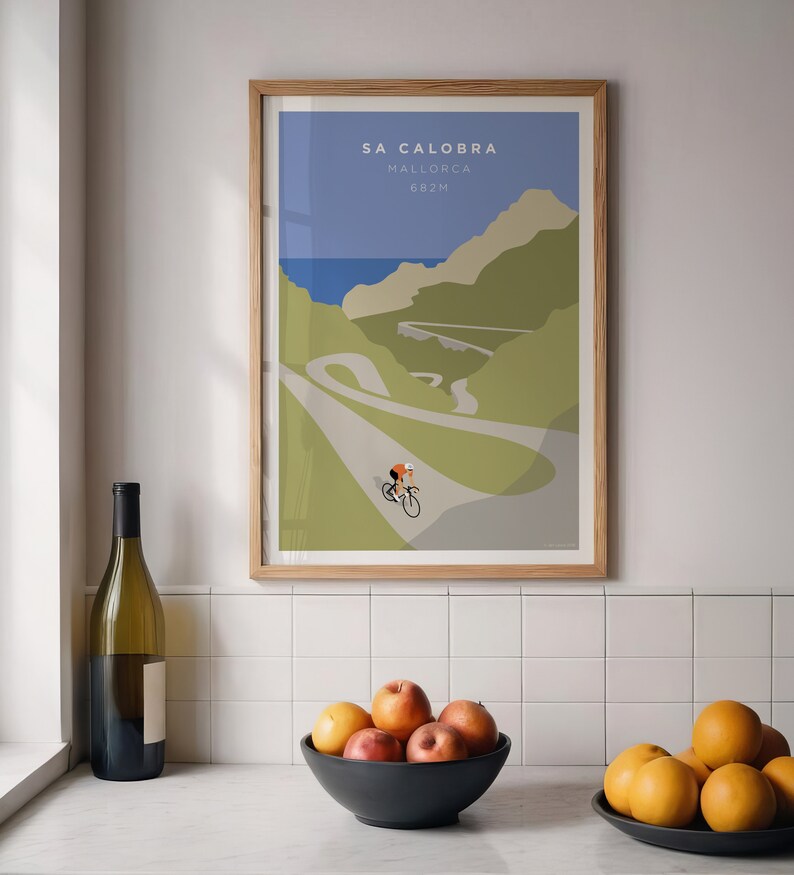 May include: A framed poster with a minimalist illustration of a cyclist riding up a winding road in the mountains. The poster is titled "Sa Calobra, Mallorca, 682m".