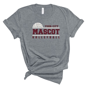 May include: Gray t-shirt with a volleyball graphic and the text "YOUR CITY MASCOT VOLLEYBALL" in maroon.