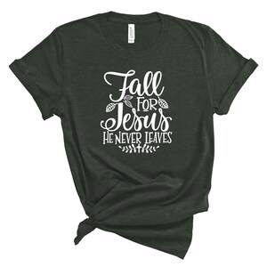 May include: A dark green t-shirt with white text that reads "Fall for Jesus He Never Leaves". The text is surrounded by small leaf designs.