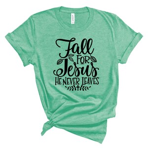 May include: A green t-shirt with the text "Fall for Jesus He Never Leaves" in black lettering. The text is surrounded by small leaf designs.