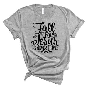 May include: Gray t-shirt with black text that reads "Fall for Jesus He Never Leaves". The text is in a decorative font with leaf accents.