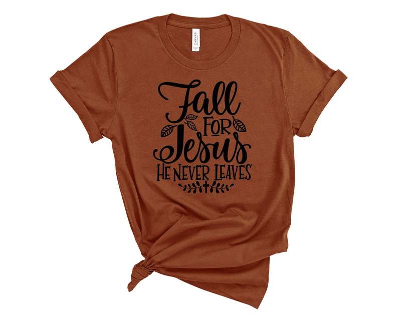 May include: A brown t-shirt with the text "Fall for Jesus He Never Leaves" in black lettering. The text is surrounded by small leaf designs.