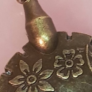 Może przedstawiać: Złoty metalowy ornament z kwiatowym wzorem. Ornament ma okrągły wierzchołek i fakturowaną powierzchnię.