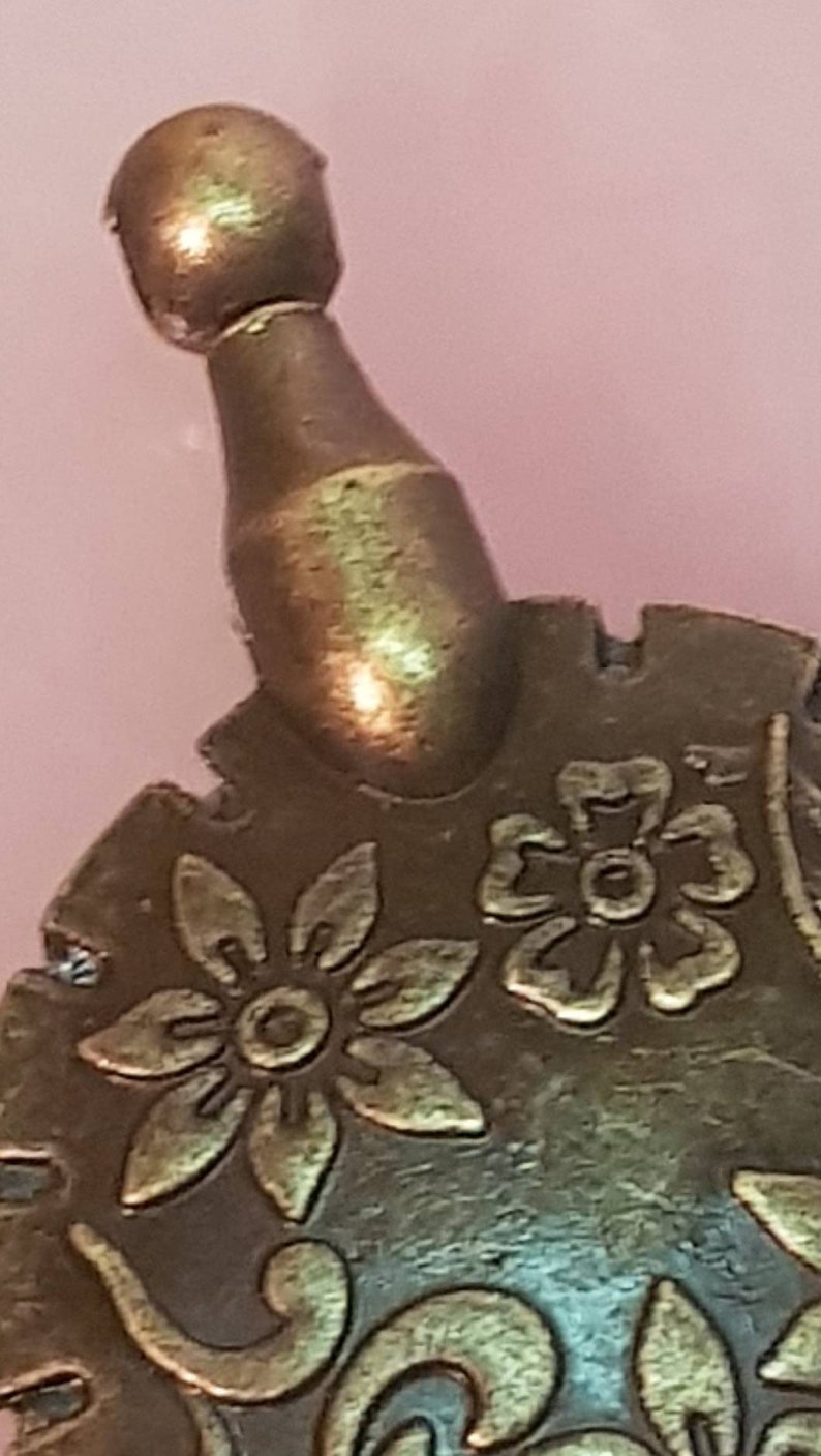 Może przedstawiać: Złoty metalowy ornament z kwiatowym wzorem. Ornament ma okrągły wierzchołek i fakturowaną powierzchnię.
