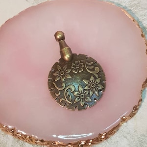 May include: A bronze-colored metal charm with a floral design. The charm has a small loop at the top for attaching to a necklace or bracelet.