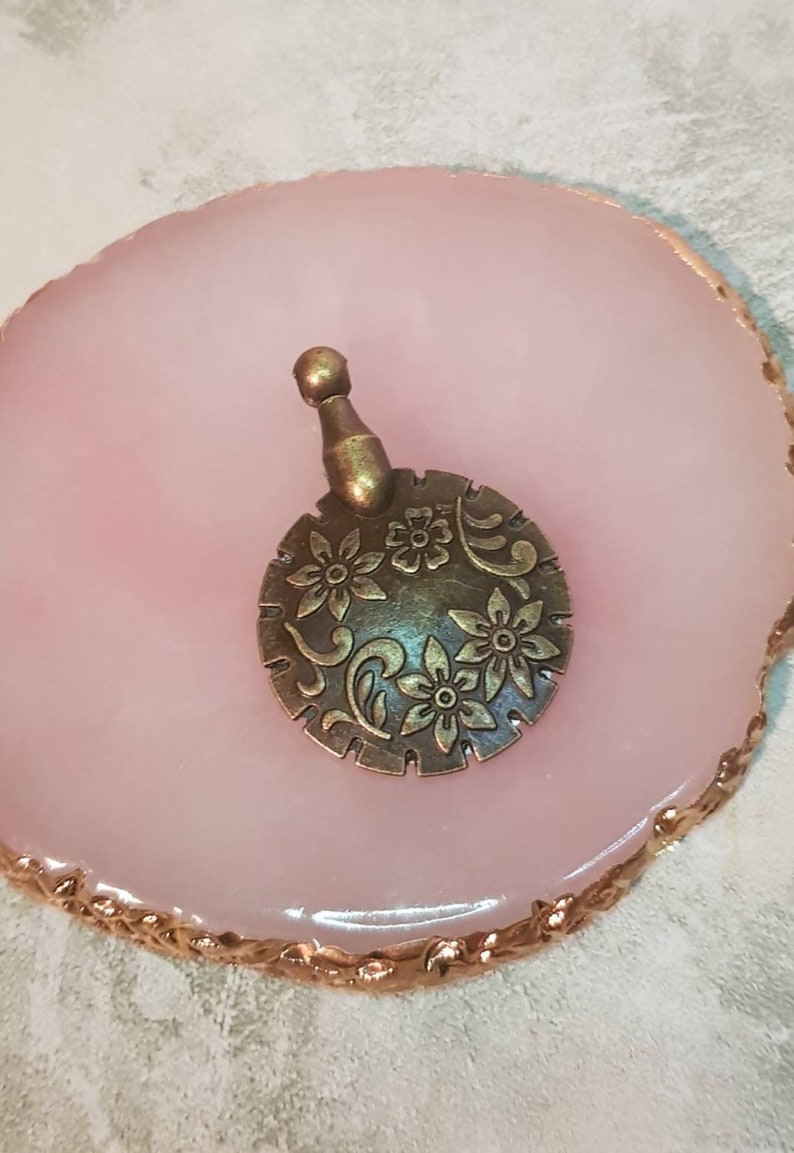 Może przedstawiać: Brązowy metalowy charm z kwiatowym wzorem. Charm ma małą pętelkę u g&oacute;ry do przymocowania do naszyjnika lub bransoletki.