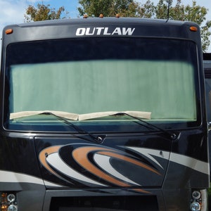 May include: A dark gray recreational vehicle with the word "OUTLAW" in white across the top. The front of the RV has a large windshield, windshield wipers, and decorative orange and white accents. Headlights are visible at the bottom.