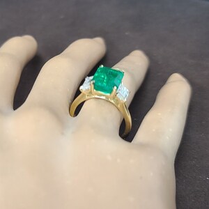 Op de afbeelding: Een gouden ring met een grote smaragdgroene edelsteen en kleinere diamant accenten.