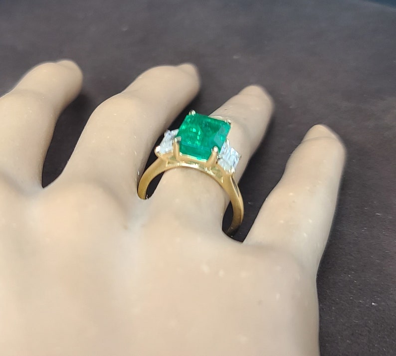 Op de afbeelding: Een gouden ring met een grote smaragdgroene edelsteen en kleinere diamant accenten.
