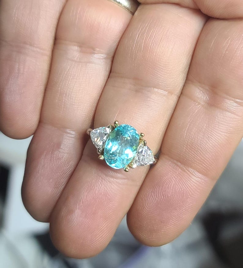 May include: A gold ring featuring a large, oval-cut, light blue gemstone flanked by two smaller, triangular, clear gemstones. The ring's setting has gold accents.