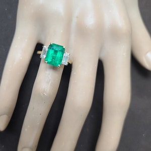 Op de afbeelding: Een gouden ring met een grote smaragdgroene edelsteen en twee kleinere baguette-geslepen diamanten aan weerszijden.