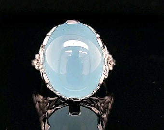 May include: A silver ring with a large, oval-shaped, light blue gemstone set in a delicate filigree design.