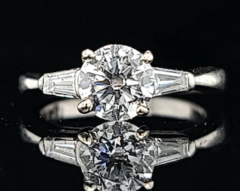 May include: A silver engagement ring with a large round center diamond and two smaller baguette diamonds on either side.