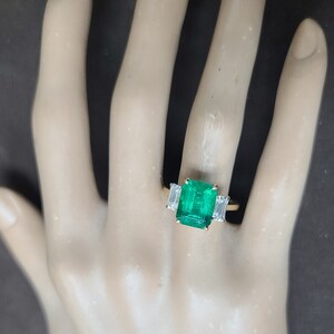 Op de afbeelding: Een gouden ring met een grote smaragdgroene edelsteen en twee kleinere baguette-geslepen diamanten aan weerszijden.