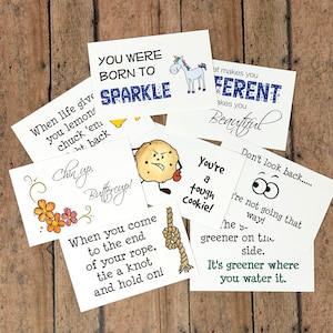 May include: A set of ten colorful cards with inspirational quotes and illustrations. The cards feature a variety of designs, including a unicorn, a cookie, a butterfly, and a rope knot. The quotes include "You were born to sparkle", "When life gives you lemons, chuck 'em back", "Chin up, Buttercup!" and "It's greener where you water it."