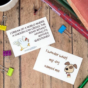 May include: Two white cards with black text and illustrations. The first card features a chicken crossing the road with the text "I dream of a world where a chicken can cross the road without having its motives questioned". The second card features a dog with the text "I wonder what my dog named me".