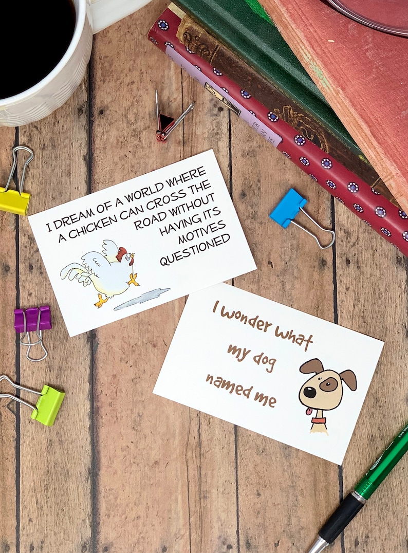 May include: Two white cards with black text and illustrations. The first card features a chicken crossing the road with the text "I dream of a world where a chicken can cross the road without having its motives questioned". The second card features a dog with the text "I wonder what my dog named me".