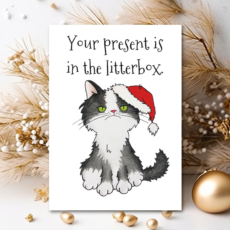 May include: A Christmas card featuring a black and white cat wearing a red Santa hat. The card reads "Your present is in the litterbox."