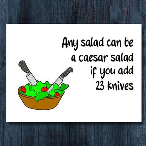 May include: A white card with the text "Any salad can be a caesar salad if you add 23 knives." The card features a cartoon illustration of a salad bowl with lettuce, tomatoes, and two knives.