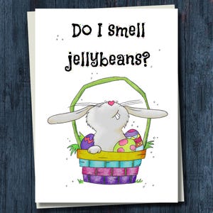 May include: Easter greeting card featuring a cartoon bunny in a basket with colorful Easter eggs. The text "Do I smell jellybeans?" is written above the bunny. The bunny has a pink heart nose and is looking up.