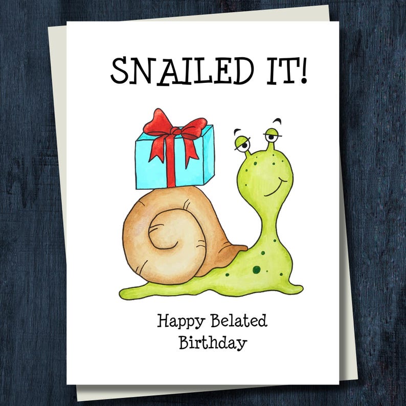 May include: A white greeting card featuring a cartoon illustration of a light green snail with a tan shell carrying a light blue gift box with a red ribbon. The text reads SNAILED IT! at the top and Happy Belated Birthday at the bottom.
