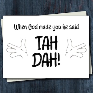 May include: A white greeting card with the text "When God made you he said TAH DAH!" in black. The card features cartoon hands on either side of the text. The card is on a cream-colored envelope.
