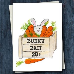 May include: A greeting card featuring a white bunny peeking out from a wooden crate filled with orange carrots. The crate has the words "BUNNY BAIT 25¢" printed on it. A single carrot is drawn below the crate.