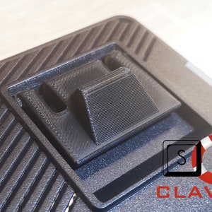 May include: Close-up of a black keyboard with a textured surface. The keyboard has a built-in stand that can be raised to adjust the typing angle. The stand is made of black plastic and has a textured surface. The keyboard also has a logo that says "CLAVIERS" with a life preserver icon.