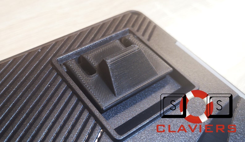 May include: Close-up of a black keyboard with a textured surface. The keyboard has a built-in stand that can be raised to adjust the typing angle. The stand is made of black plastic and has a textured surface. The keyboard also has a logo that says "CLAVIERS" with a life preserver icon.