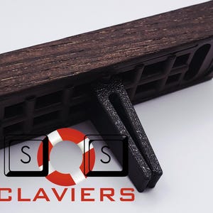 Op de afbeelding: Een donkerbruine houten polssteun voor een toetsenbord met een zwarte standaard. De steun heeft een textuuroppervlak en een rechthoekige vorm. Het logo "S" en "CLAVIERS" is zichtbaar.