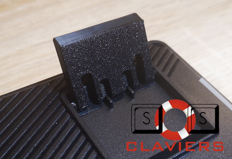 May include: Black keyboard wrist rest with a textured surface and a black plastic stand with three slots. The stand is attached to the wrist rest and can be raised to elevate the keyboard.