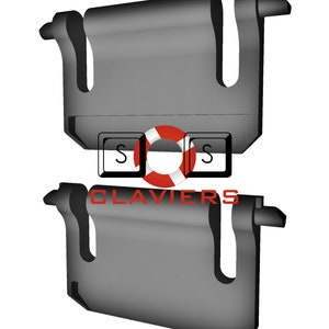 Puede incluir: Dos clips de plástico negro con un diseño en forma de U. Los clips están apilados uno encima del otro. El texto "CLAVIERS" está impreso en rojo en el clip inferior.